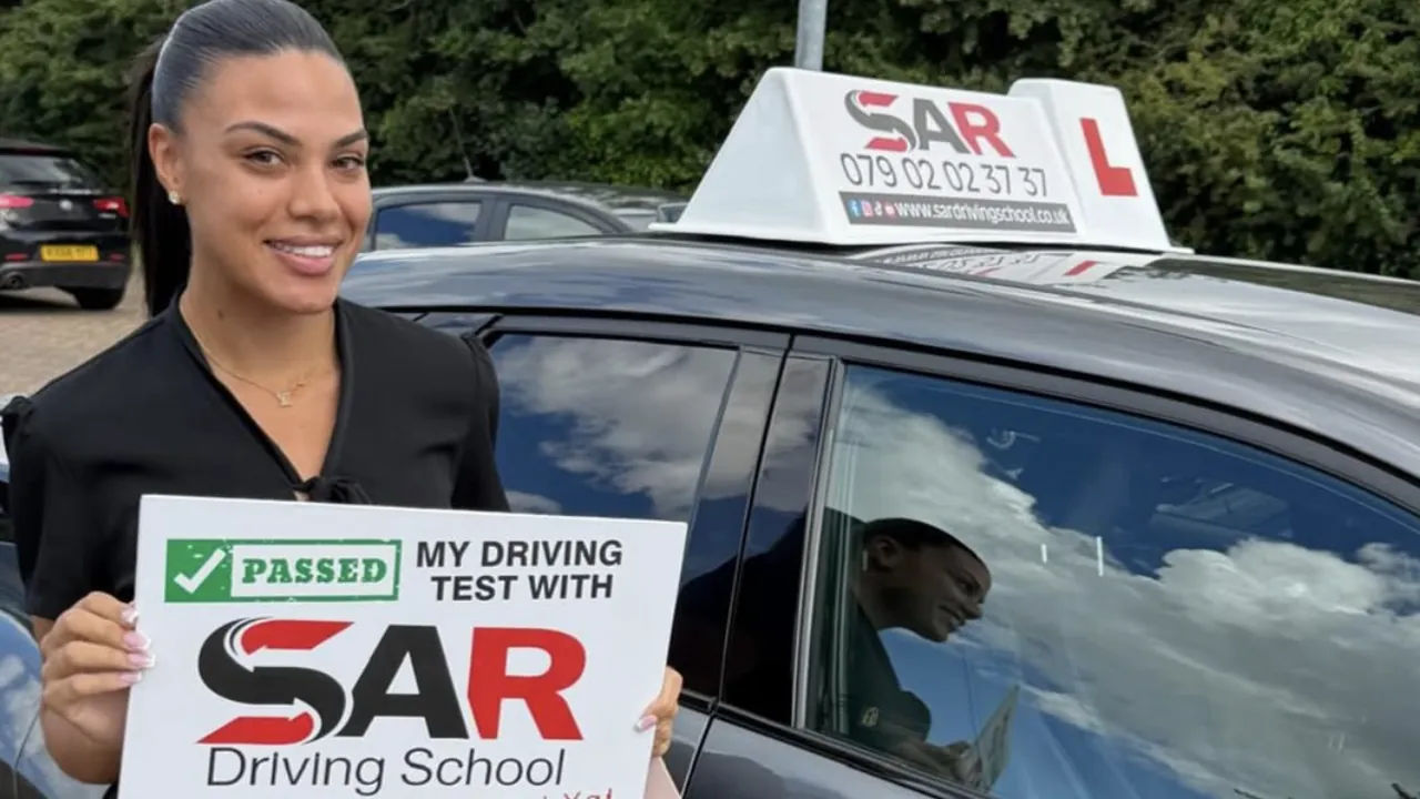 A SAR Driving School pupil holding their pass certificate beside a SAR tuition car