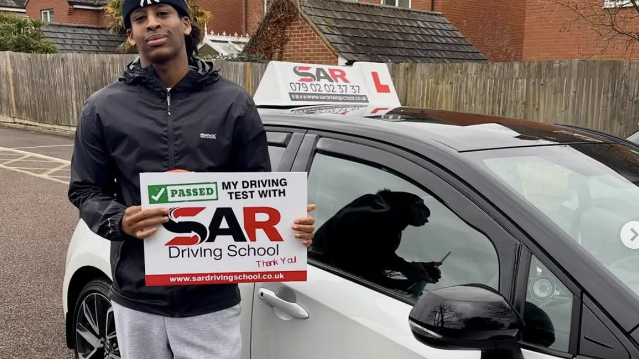 A SAR Driving School pupil holding their pass certificate beside a SAR tuition car