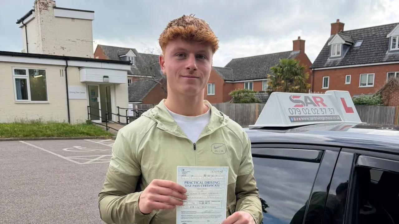 A SAR Driving School pupil holding their pass certificate beside a SAR tuition car